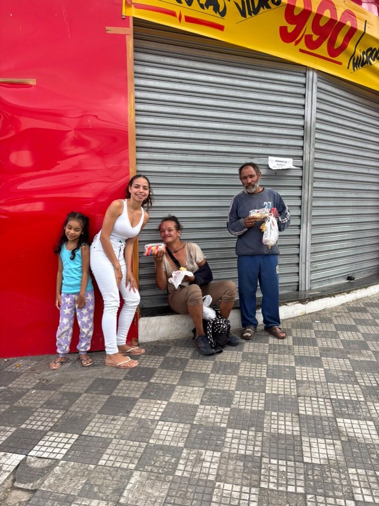 Uma moça e uma menina junto de duas pessoas que receberam lanches, em frente a uma loja